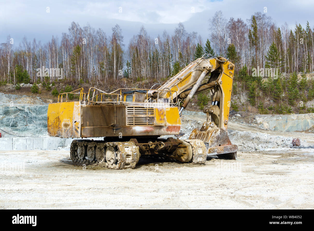 yellow dirty excavator stands in a quarry for the extraction of marble