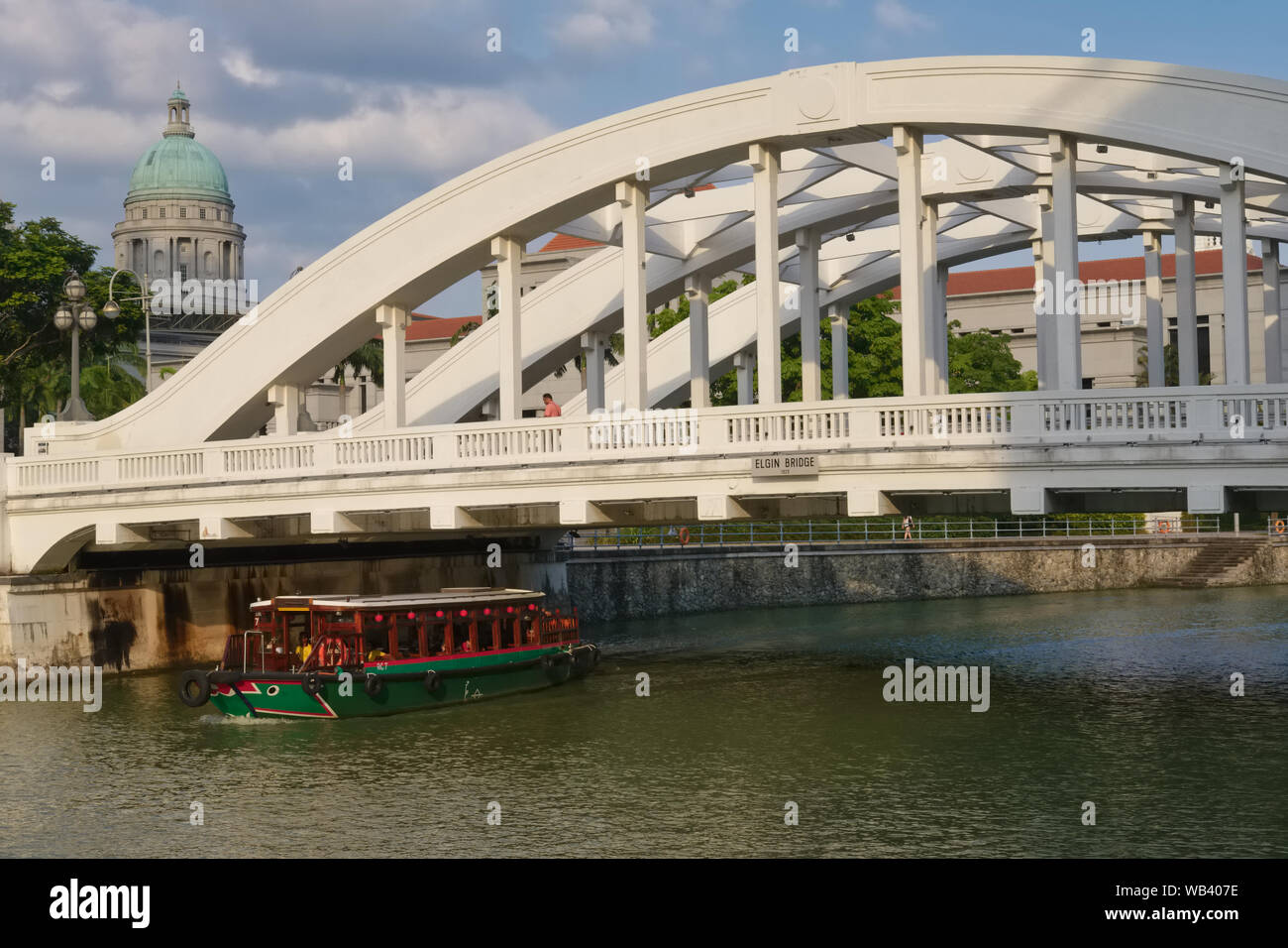 A tour boat on the Singapore River, Singapore, passes under colonial-era Elgin Bridge, the dome of the National Gallery Singapore seen in the b/g Stock Photo