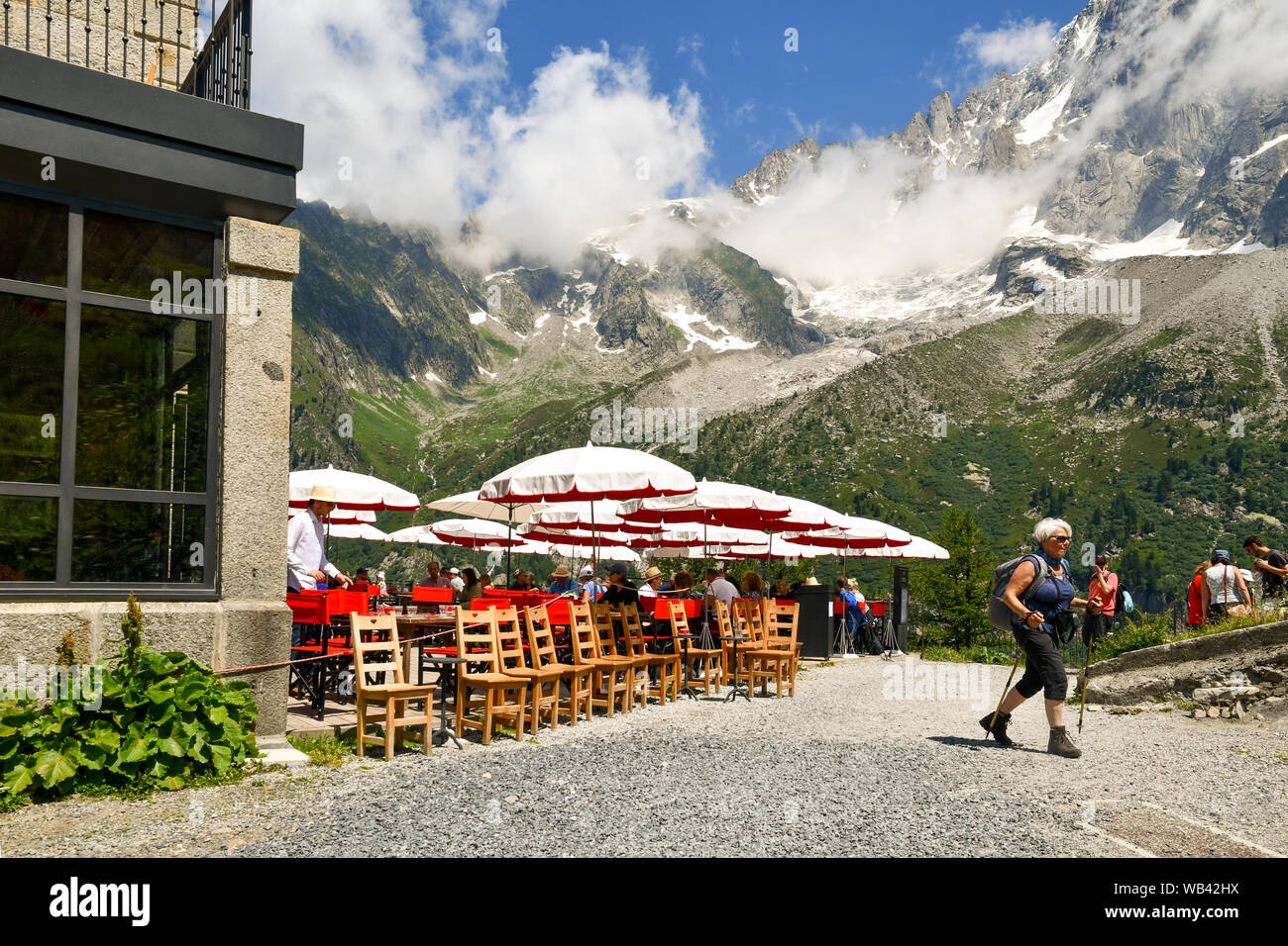 Outdoor café of Refuge of Montenvers with tourists, an elderly lady doing Nordic walking and Aiguilles du Dru mountain, Chamonix-Mont-Blanc, France Stock Photo