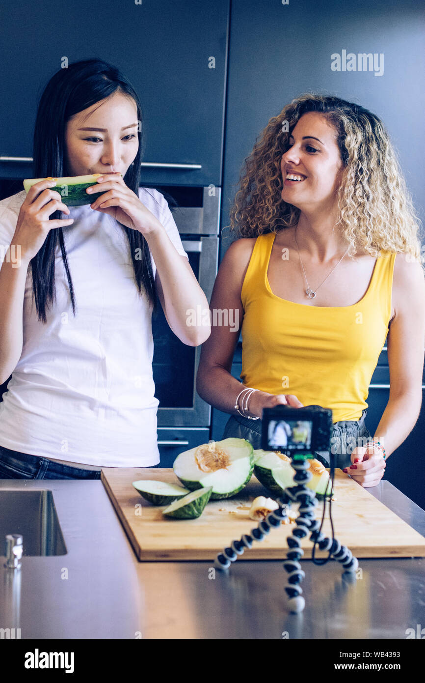 Asian young girl tasting a piece of melon, another smiling young woman is cutting the melon while they are recording with a camera Stock Photo