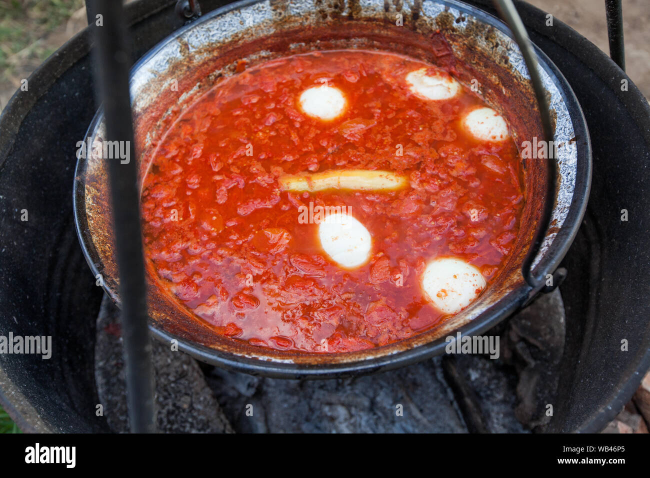 Preparing homemade organic tomato juice in big steel kettle over fire