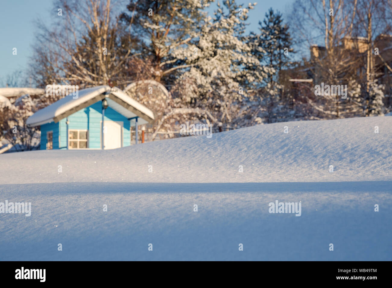 Winter landscape. Drifts of snow sparkling in the sun against a blurred background of a small house and trees covered with snow. Shallow depth of fiel Stock Photo
