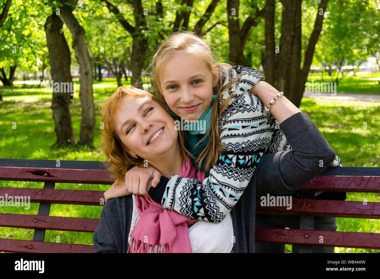 teen daughter walks up behind her mother sitting on a park bench and ...