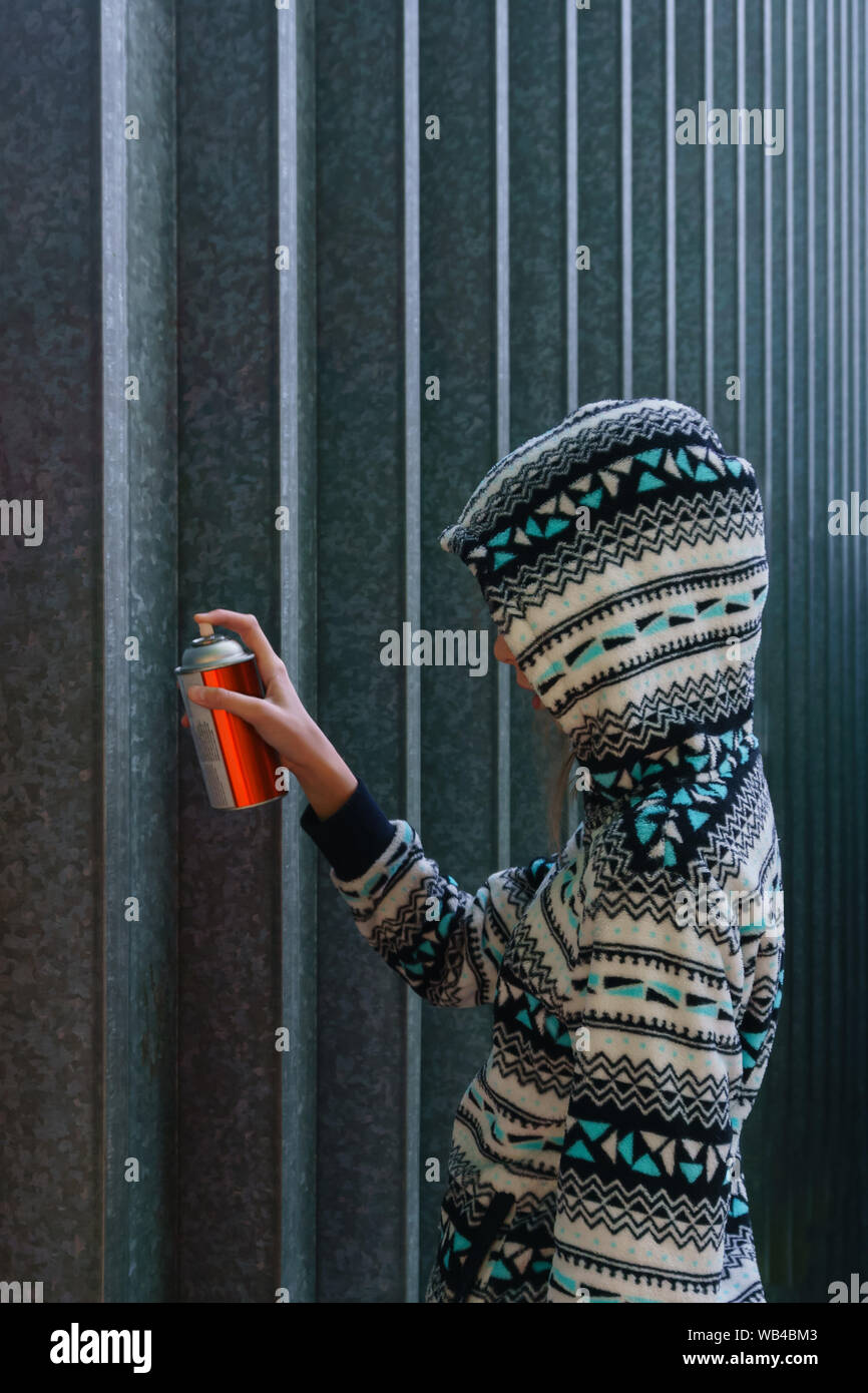 teen girl with spray paint looks around, about to write graffiti on the wall Stock Photo