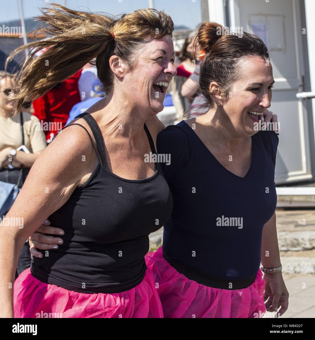 Sidmouth, 24th Aug 19 Two girls try to decide whether to enter the three legged race in the Bank Holiday sun at Sidmouth, Devon. Runners had to visit 6 pubs, and drink a half pint in each during the event. Credit: Photo Central/Alamy Live News Stock Photo