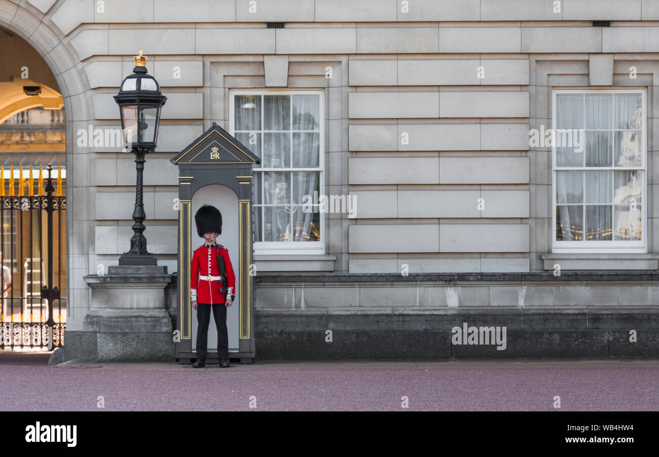 Soldier from Queen's Guard wearing red tunic & bearskin hat in sentry box at Buckingham Palace in City of Westminster, City of London, UK. Stock Photo