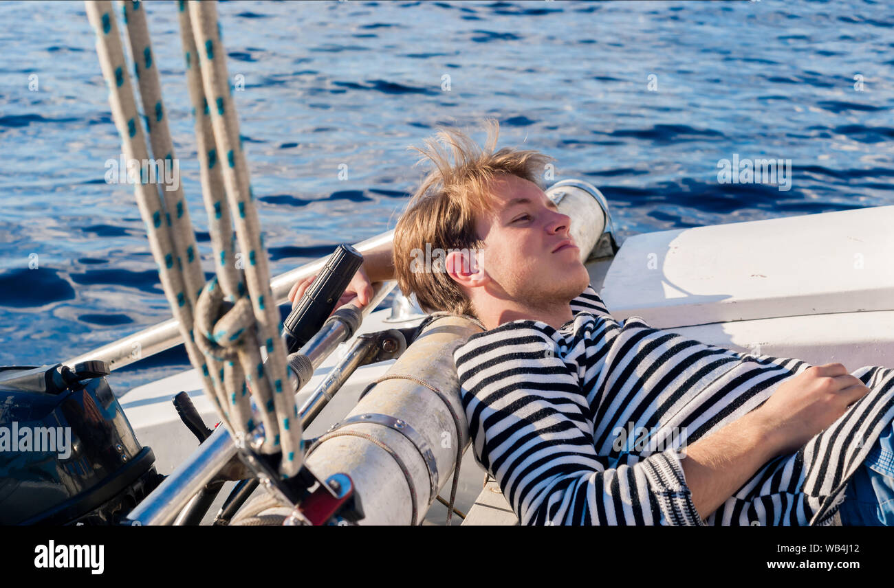 young male yachtsman resting aft of the yacht on a sunny day during forced inactivity during calm weather Stock Photo