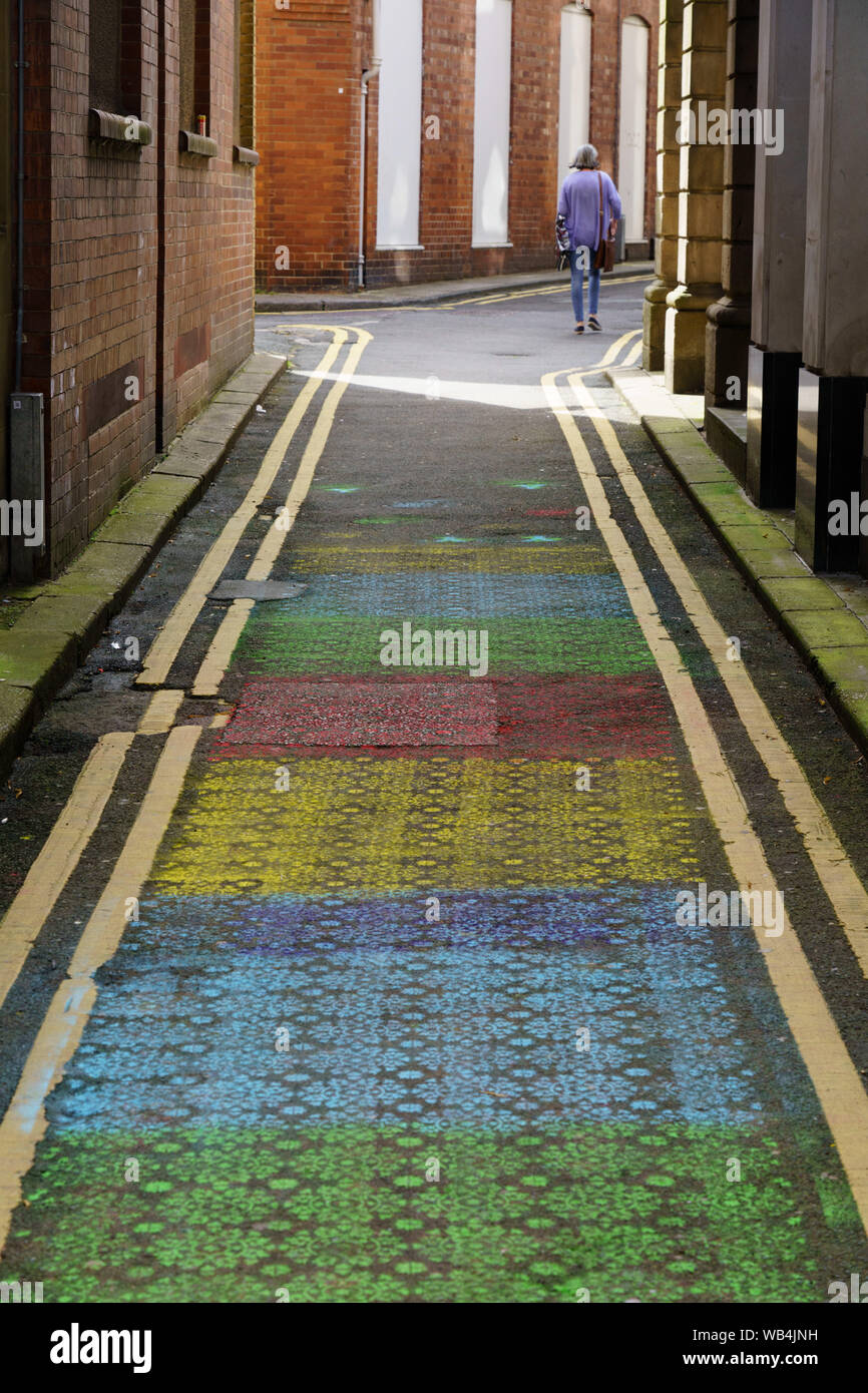 Woman walking along a narrow road decorated with colourful stencil patterns, Harrogate, North Yorkshire, England, UK. Stock Photo
