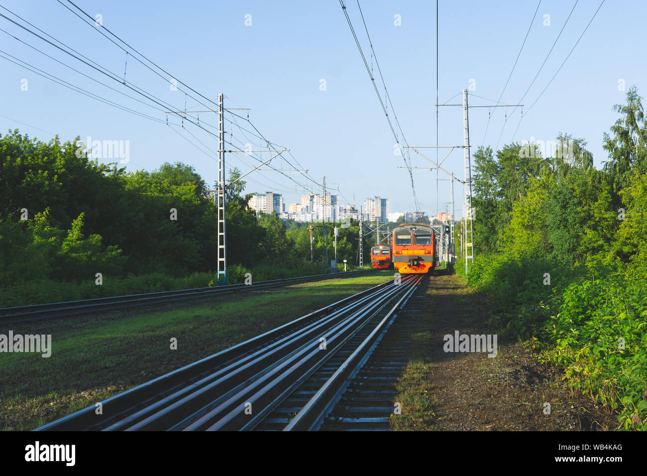 morning suburban landscape with two oncoming electric commuter trains and city on a hill in the distance Stock Photo