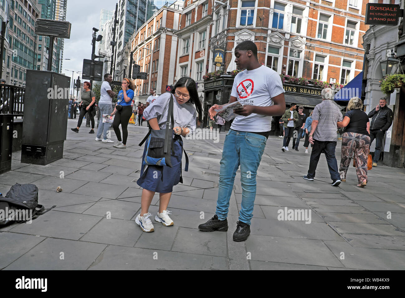 Young woman reaching for purse in handbag to make donation to young man fundraising for education in Liverpool Street London England UK  KATHY DEWITT Stock Photo