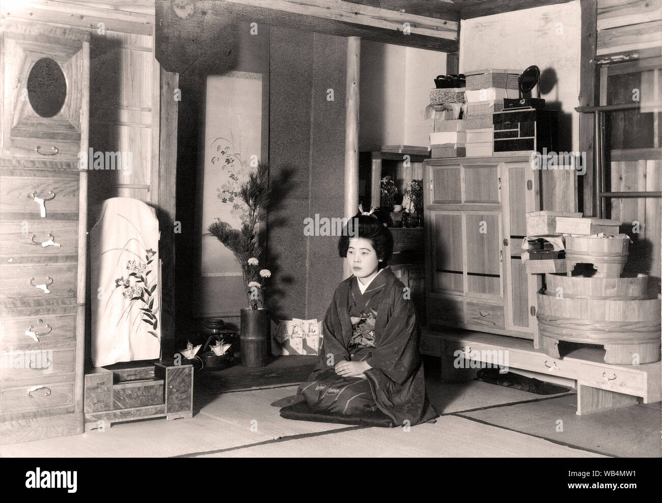 [ 1920s Japan - Japanese Bride with Trousseau ] —   A young woman in kimono sits in a room full of items that appear ready to be moved to a new home. Until the late 21st century it was customary to move new furniture ceremoniously to a newly married couple’s home.  20th century vintage gelatin silver print. Stock Photo