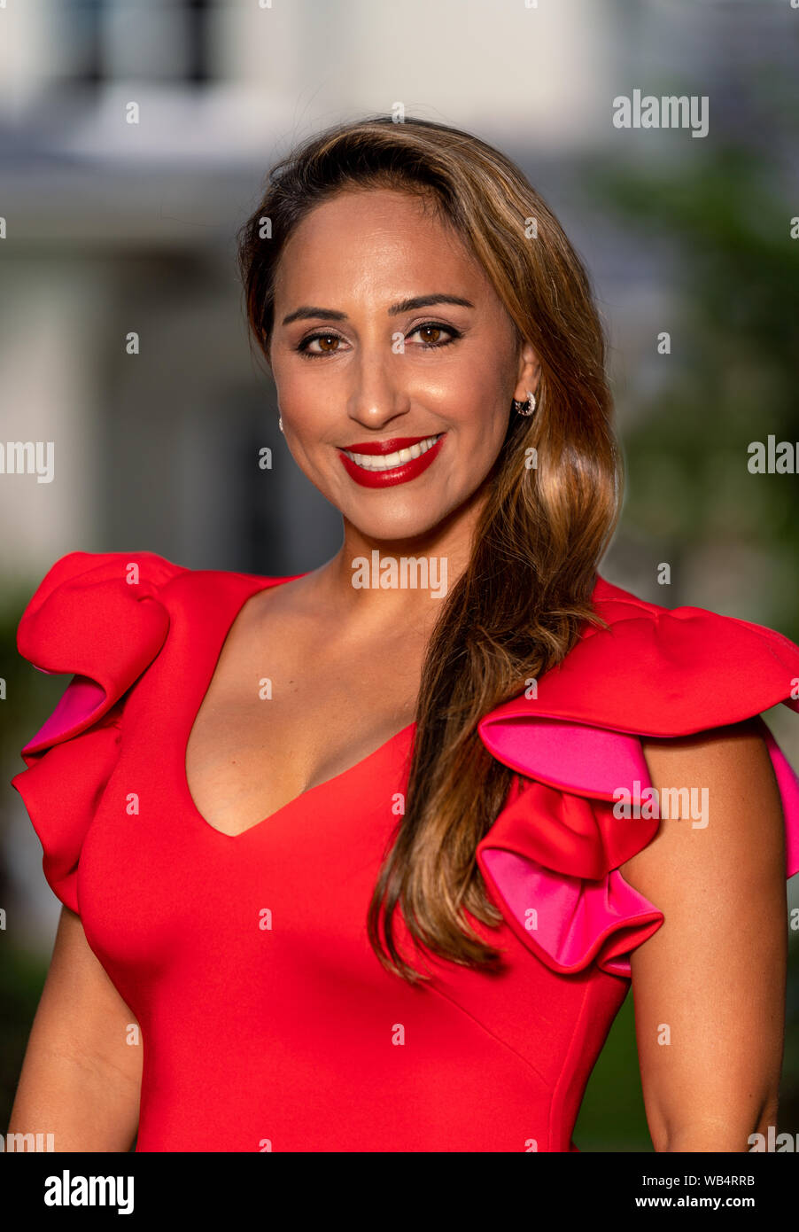Portrait of a mixed race business woman smiling in red dress outside with a house in the background Stock Photo