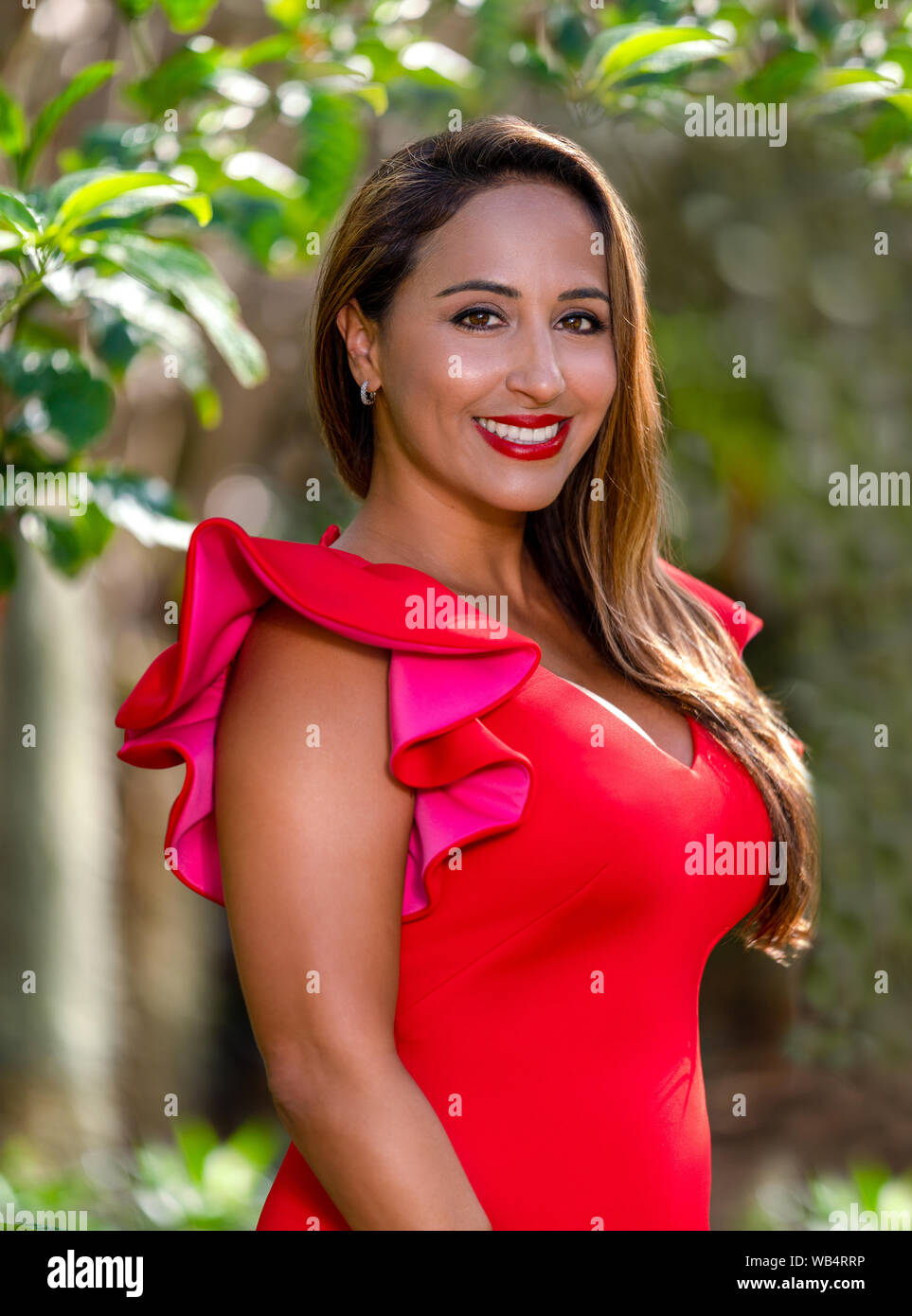 Portrait of a mixed race business woman smiling in red dress outside Stock Photo