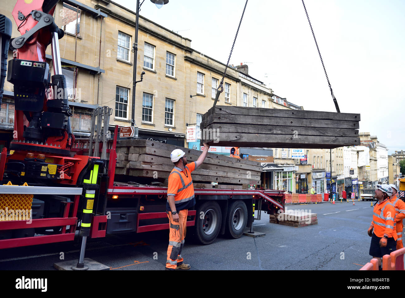 Mobile crane lifting wood blocks off lorry on city street Stock Photo