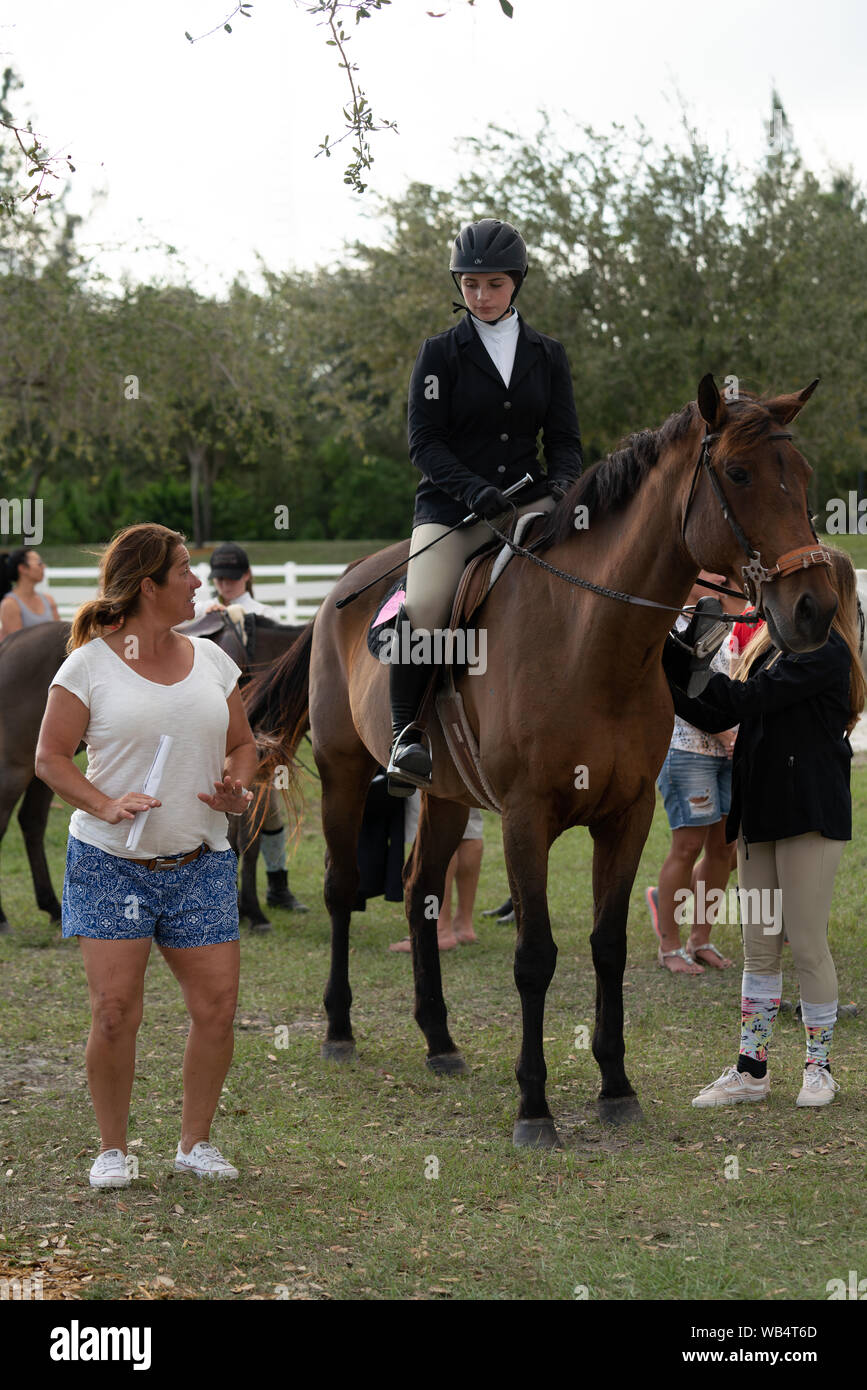 A female riding instructor is demonstrating to her student proper