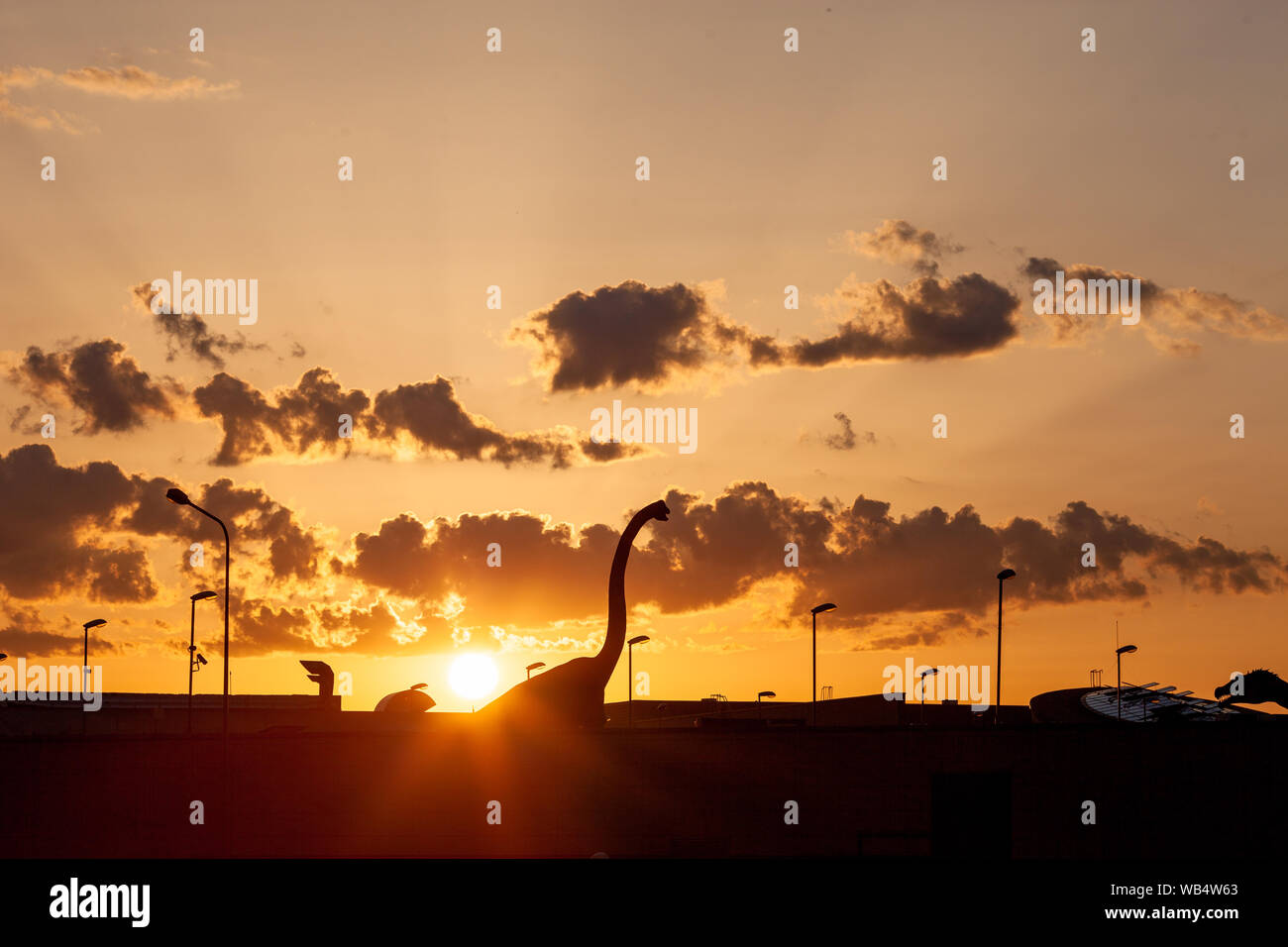 Sauropod dino coming to the city. A silhouette of herbivores dinosaur in the town with a dramatic sky behind. Stock Photo