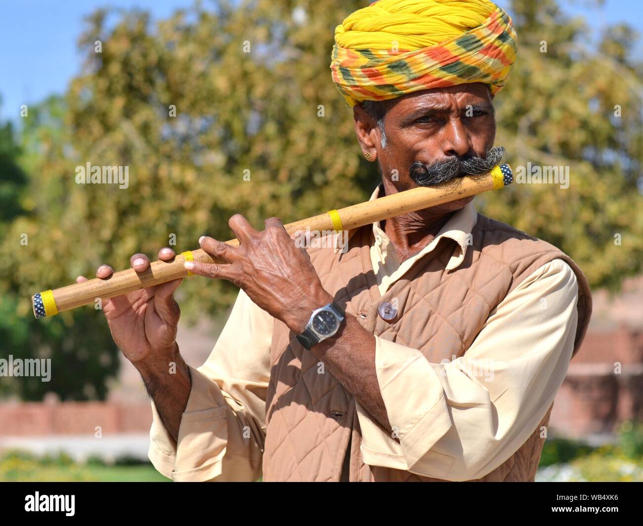 Indian bansuri player (traditional transverse flute) with yellow Rajasthani turban plays outdoors on his instrument. Stock Photo