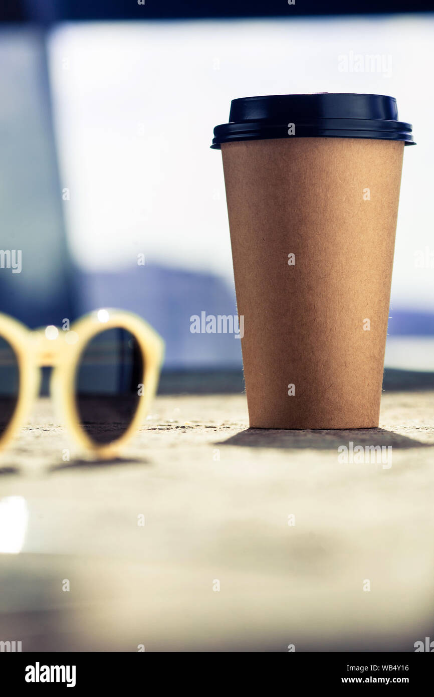 Disposable coffee cup on the rough table next to sunglasses. Sunny summer morning and holiday mood. Stock Photo