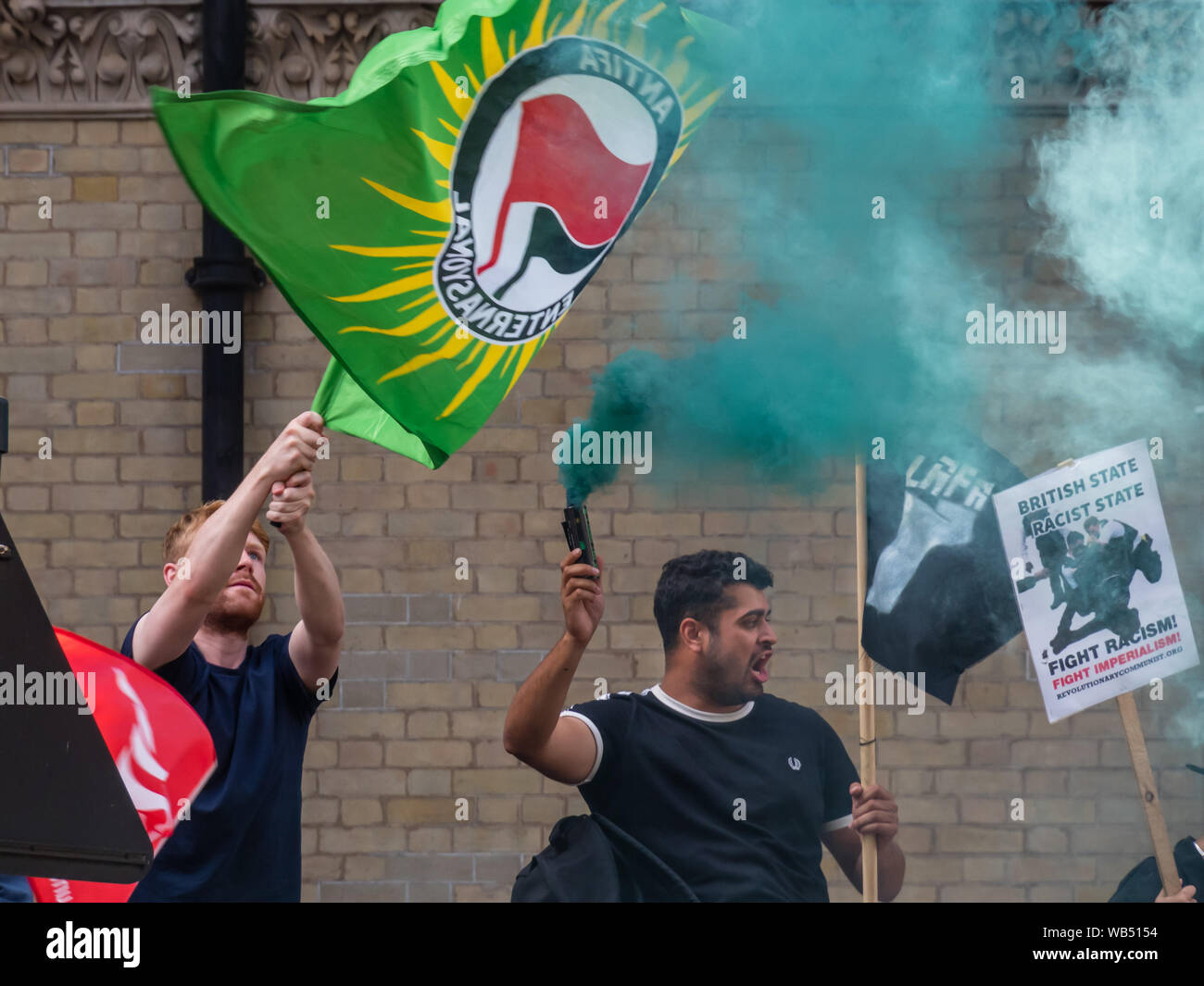 London, UK. 24th August 2019. Anti-fascists hold flags and flares as they oppose a protest at the BBC by Tommy Robinson supporters who claim he is in jail for journalism. He was sentenced to 9 months for 3 offences outside Leeds Crown Court which could have led to the collapse of a grooming gang trial, and has previous convictions for violence, financial and immigration frauds, drug possession and public order offences. Police kept the two groups apart. Robinson supporters were later joined by marchers from Trafalgar Square, and a larger group from Stand Up to Racism came to join Antifa. Peter Stock Photo
