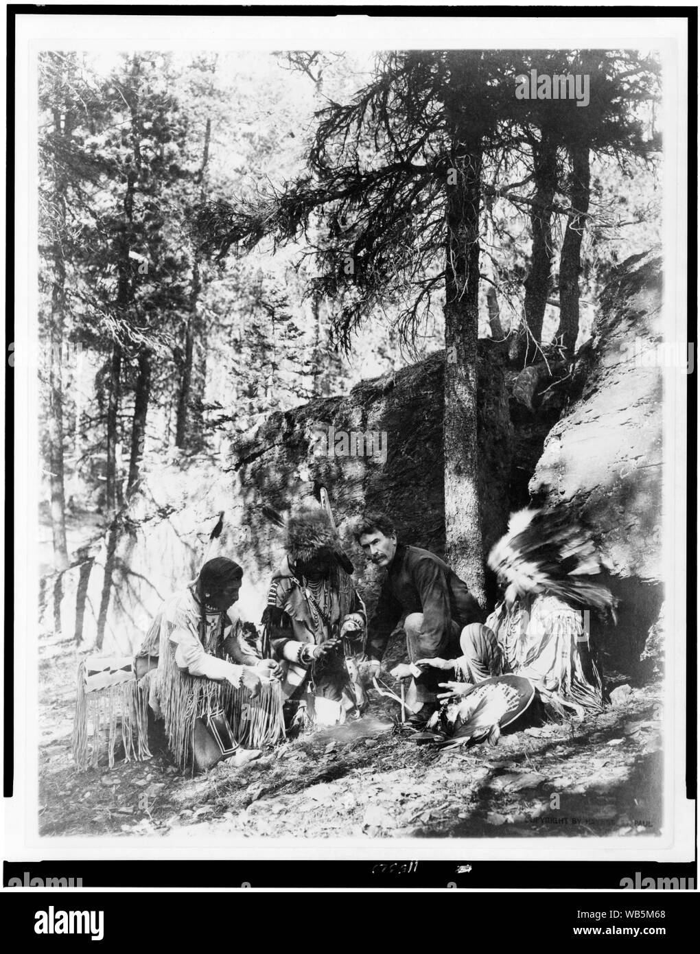 Ernest Thompson Seton, with three Blackfeet Indians, demonstrating how to start a fire using a bow and a stick, rocks and trees in background Abstract/medium: 1 photographic print. Stock Photo