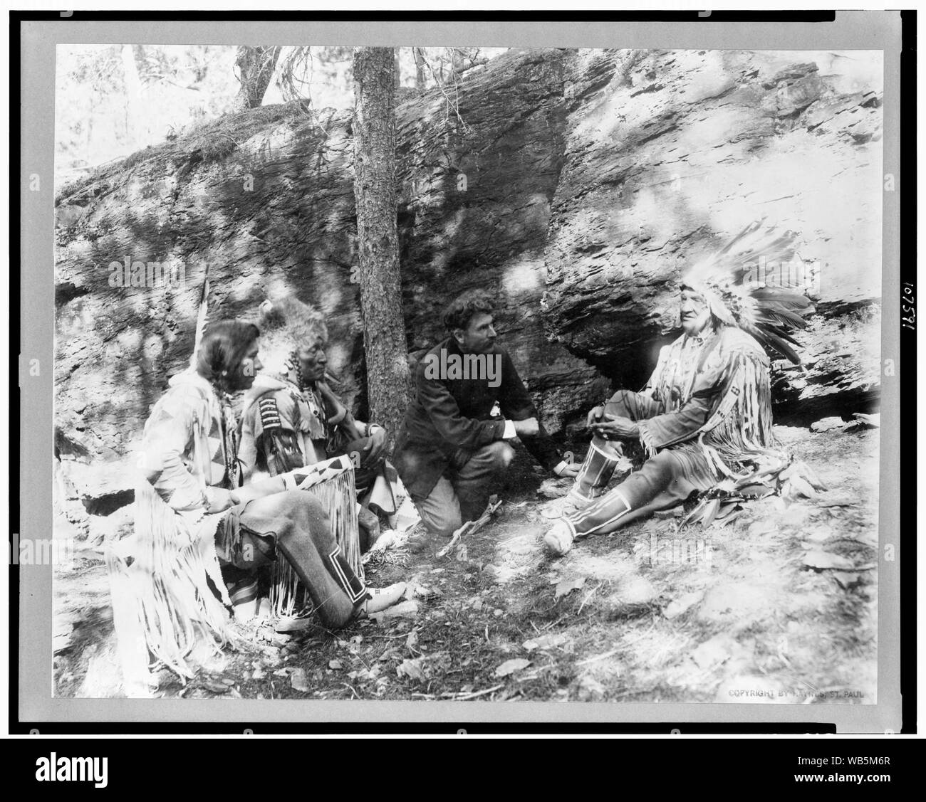 Ernest Thompson Seton, with three Blackfeet Indians, demonstrating how to start a fire using a bow and a stick, rocks and trees in background Abstract/medium: 1 photographic print. Stock Photo