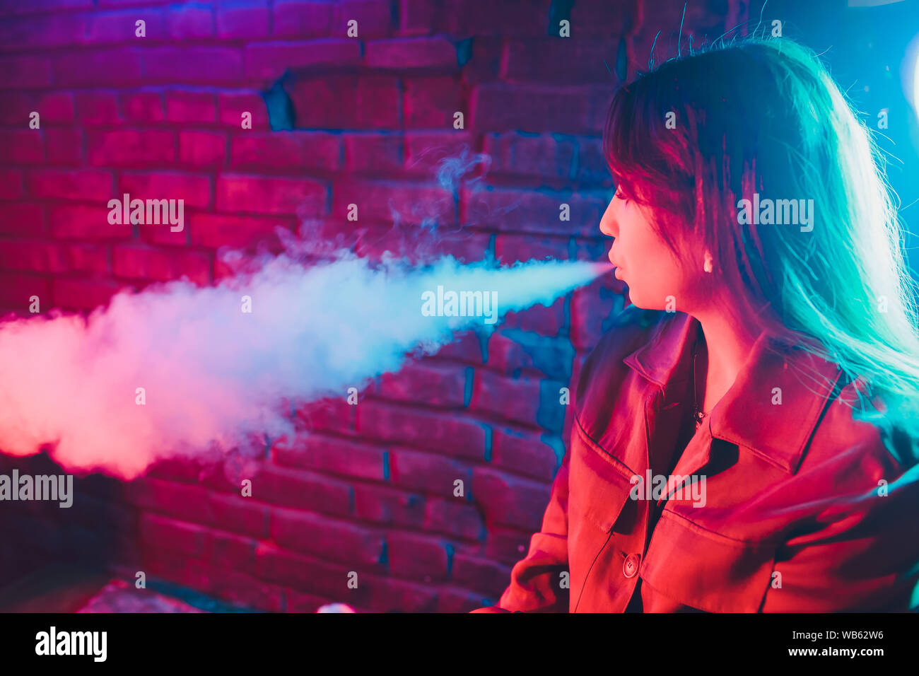 woman smokes a e-cigarette lying on the bed in the room. Smoker's concept Vaping Stock Photo