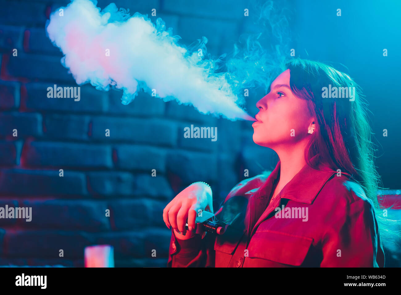 woman smokes a e-cigarette lying on the bed in the room. Smoker's concept Vaping Stock Photo