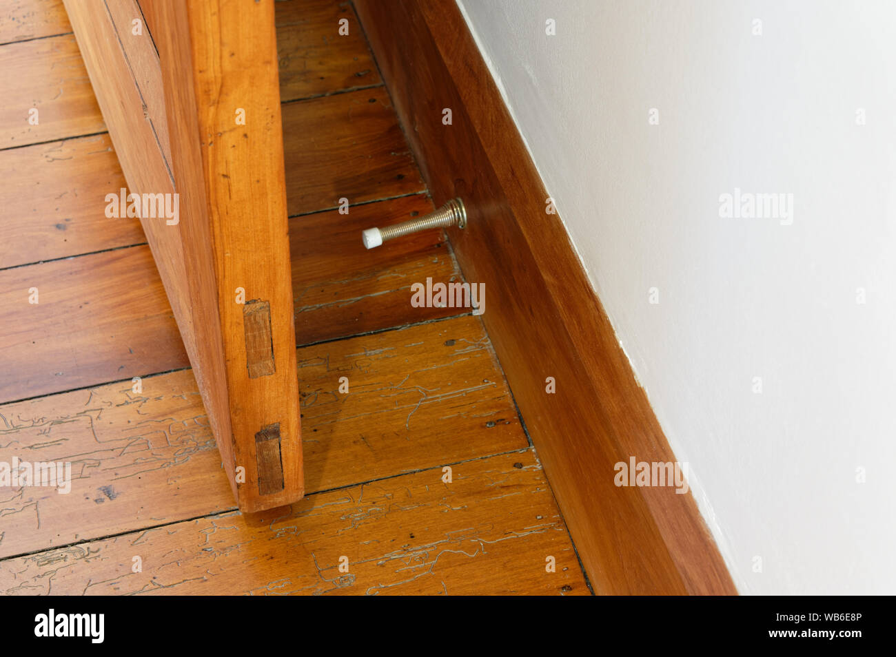 A spring door stopper is attached to a wooden skirting board to prevent the door from hitting the wall Stock Photo