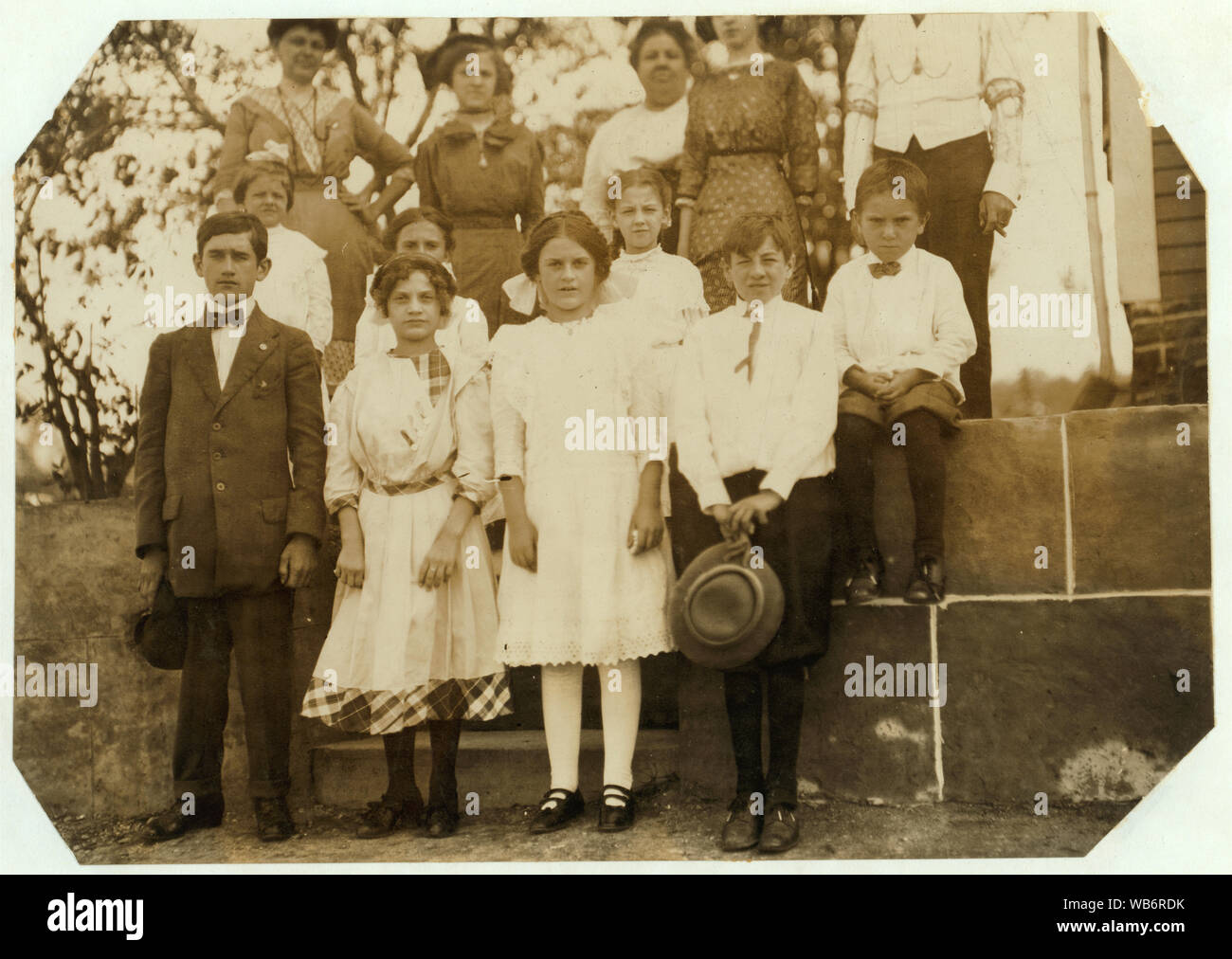 Family of Ida Descheues [?], 80 Wear Street. She is the third girl in the front of the picture, her sister--taller than she--next to her said--13 years old--but I doubt it. Ida has half hours ride in crowded stuffy cars to and from work each day. Leaving home at 6 A.M. and returning at 6:30 P.M. The doffing work in much of it standing, stooping and reaching. Bad for adolescent girl. Abstract: Photographs from the records of the National Child Labor Committee (U.S.) Stock Photo