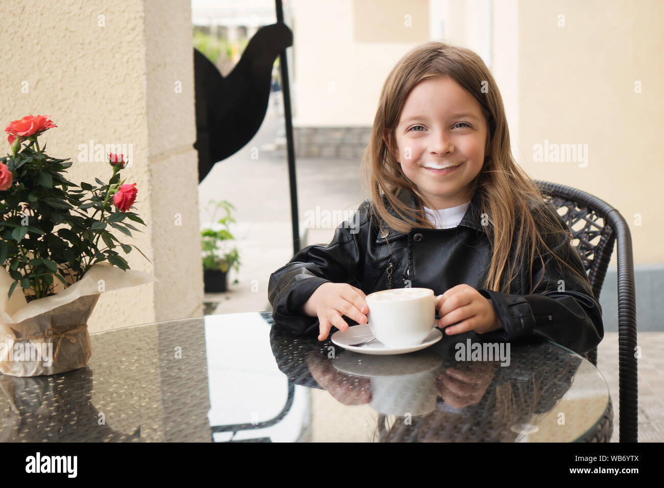 Little prankster schoolchild enjoys a coffee drink. She is pleased and happy. Milk foam on his face as the mustache. Incredibly delicious Stock Photo