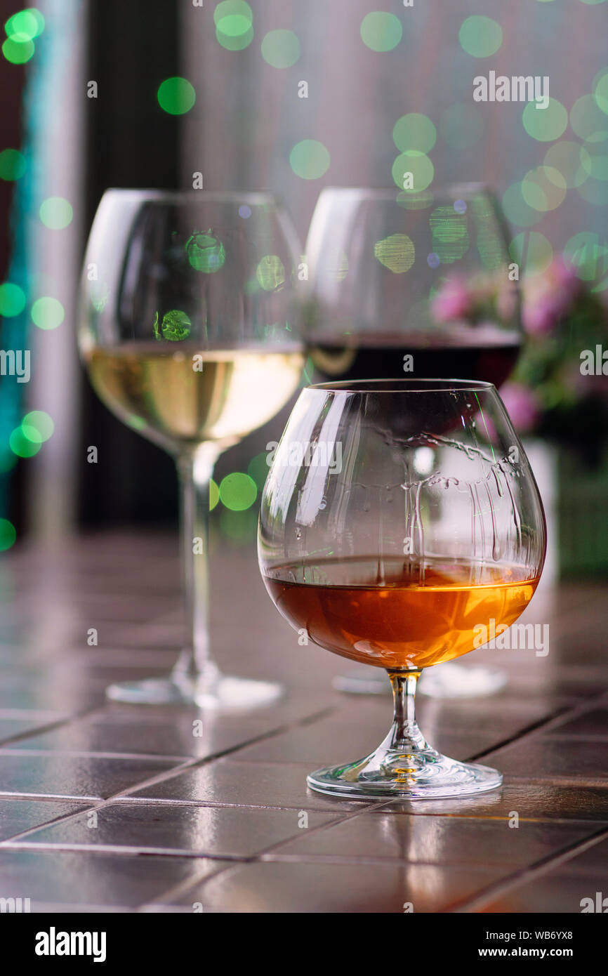 Brandy in typical snifter. Cognac in elegant glass with space for text on colorful background. Two glasses of wine in background unfocus. Tasting, res Stock Photo