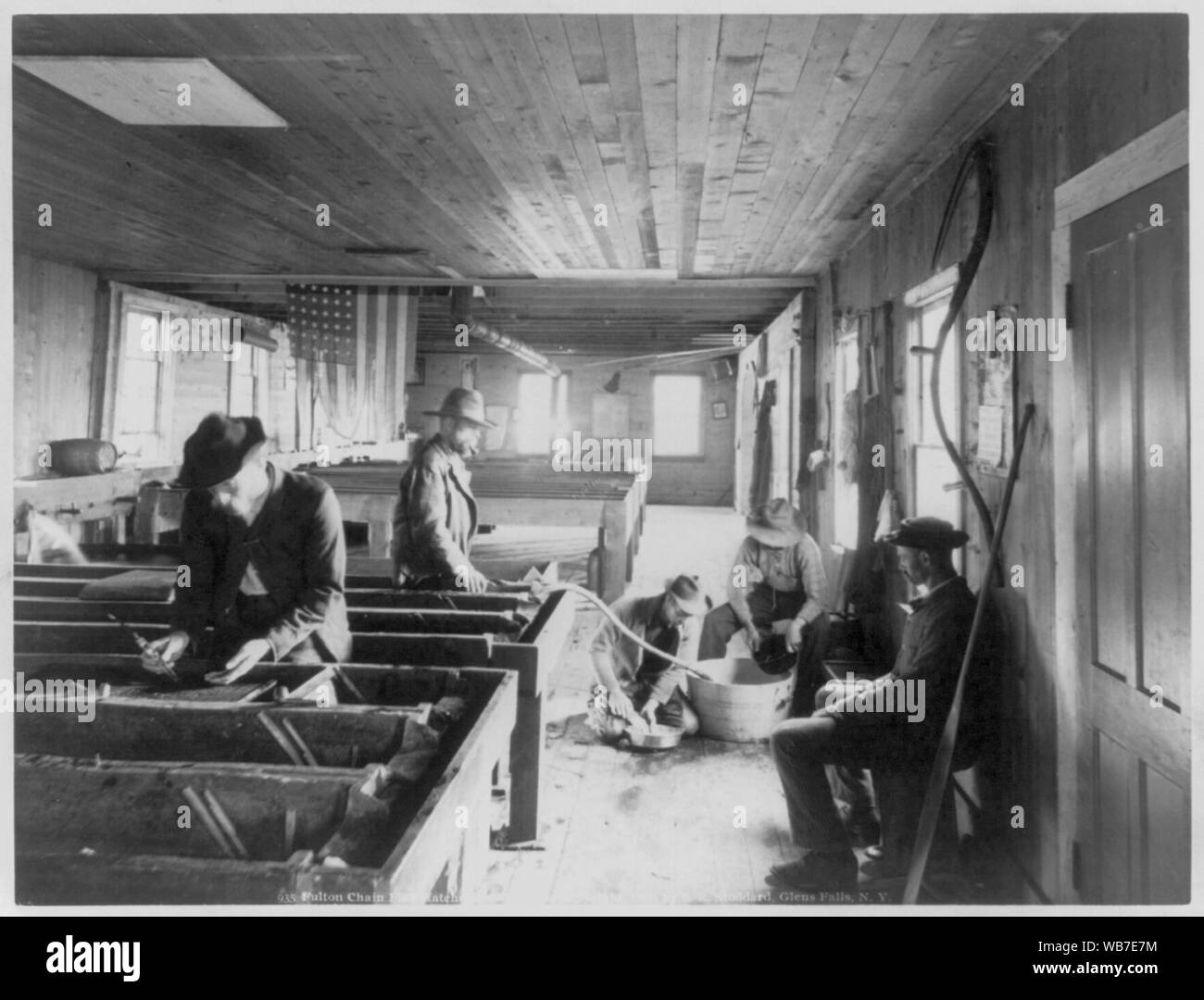 Five men in Fulton Chain Fish Hatcher, Old Forge, N.Y. Tattered U.S. flag hanging from ceiling Abstract/medium: 1 photographic print. Stock Photo