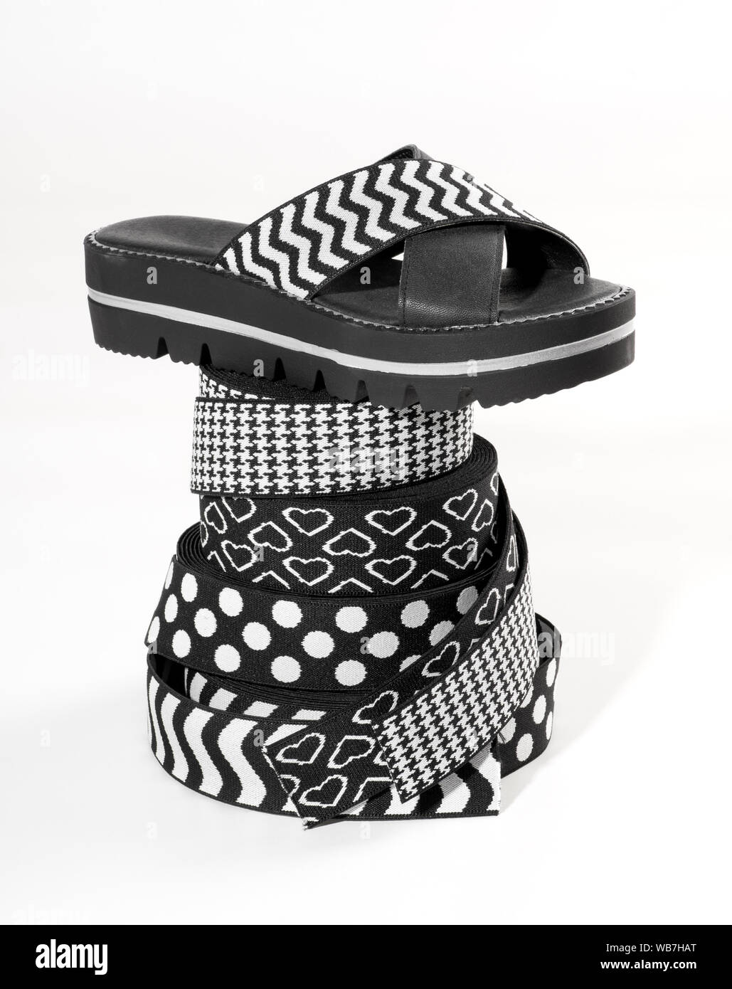 Summer sandal with crossed boldly patterned black and white elastic bands for uppers displayed balanced on a stack of decorative rolls of elastic with Stock Photo
