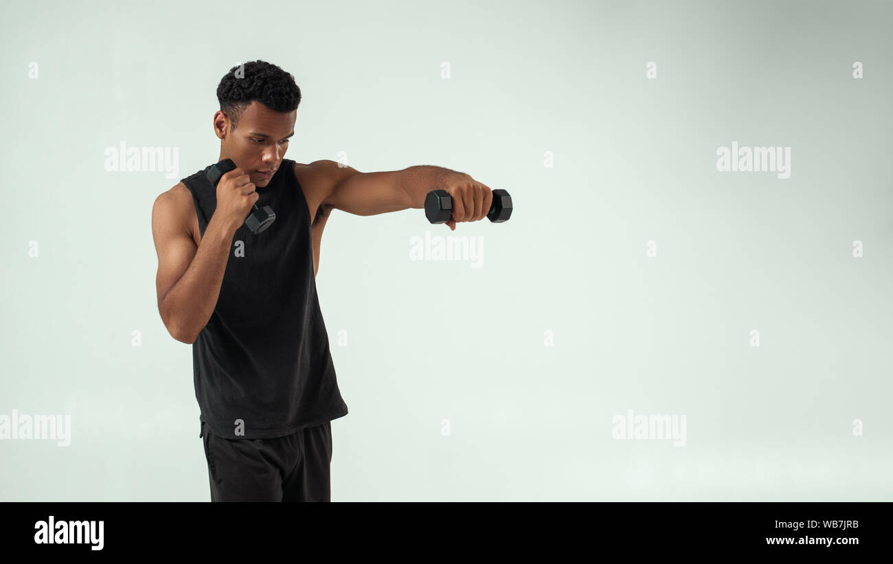Perfect biceps. Muscular young african man exercising with dumbbells while standing against grey background. Studio shot. Sport concept Stock Photo