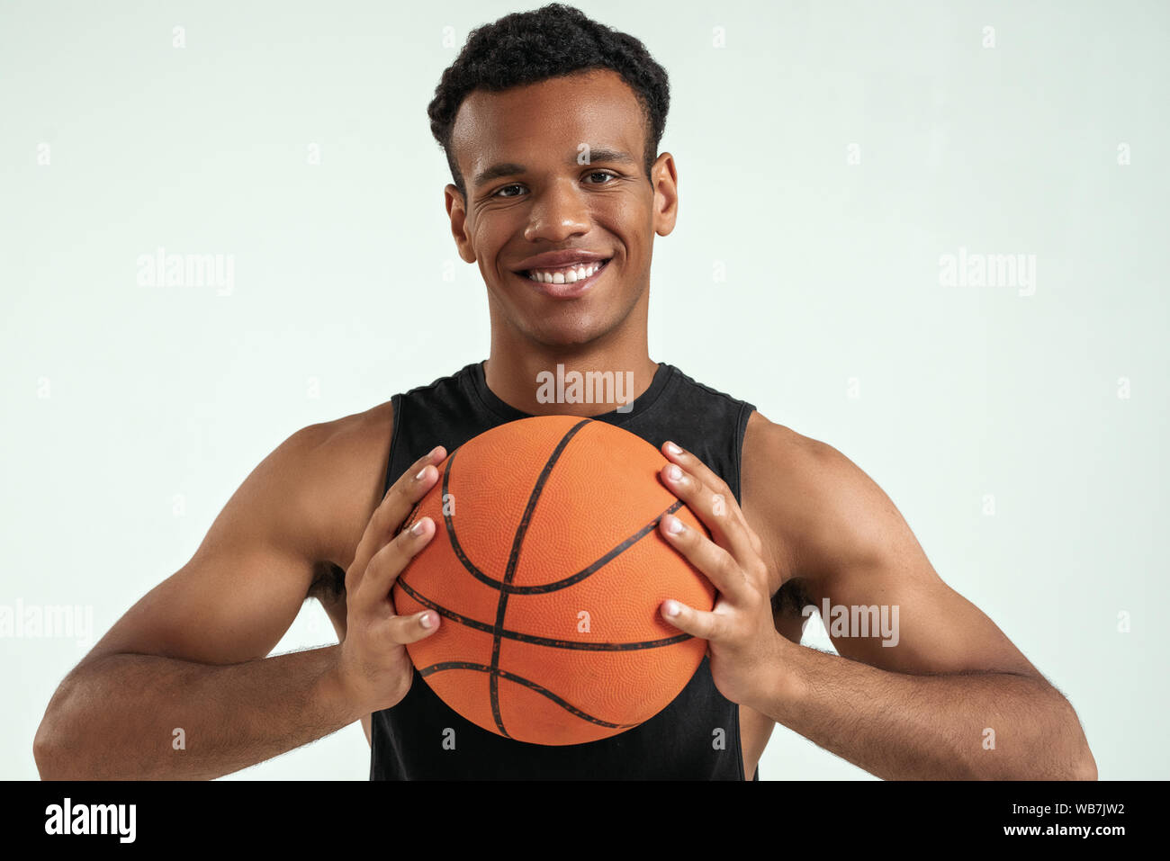Full of energy. Young smiling african man holding basketball ball and