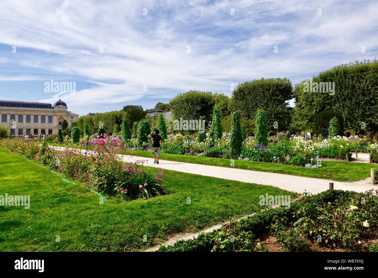People enjoying bright, summer flowers in the gardens of the Jardin des Plantes, Muséum National d'Histoire Naturelle in the background, Paris, France Stock Photo