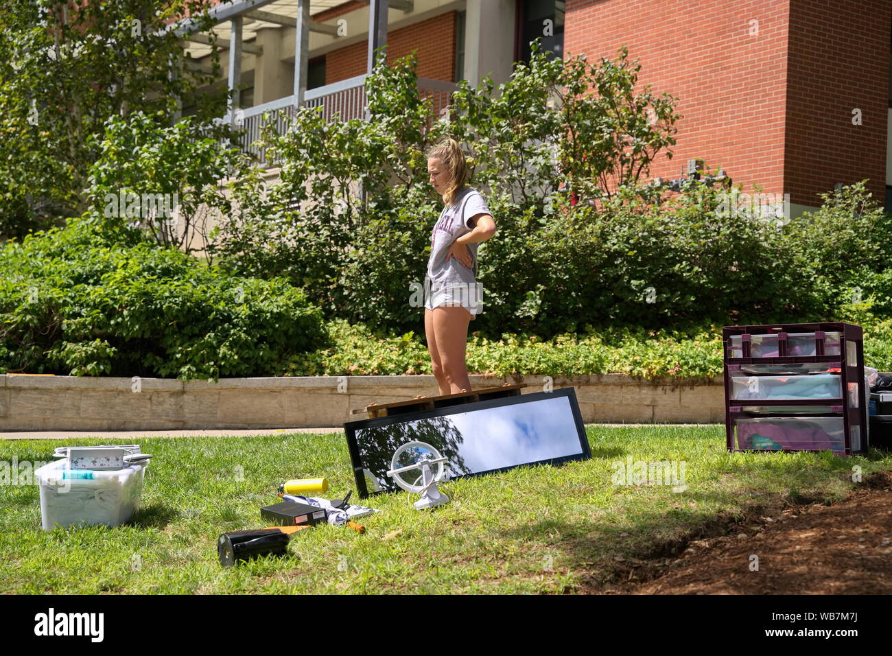 Storrs, CT USA. Aug 2019. Lone female coed with supplies all over the lawn taking a break from moving in to her new dorm. Stock Photo