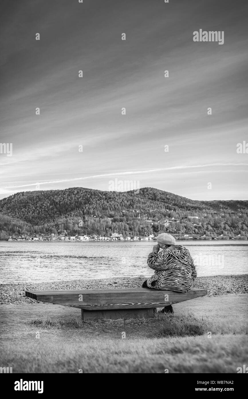 the old grandmother is sad and crying on the Bank of a beautiful river. black and white dramatic photo. veertical viev Stock Photo