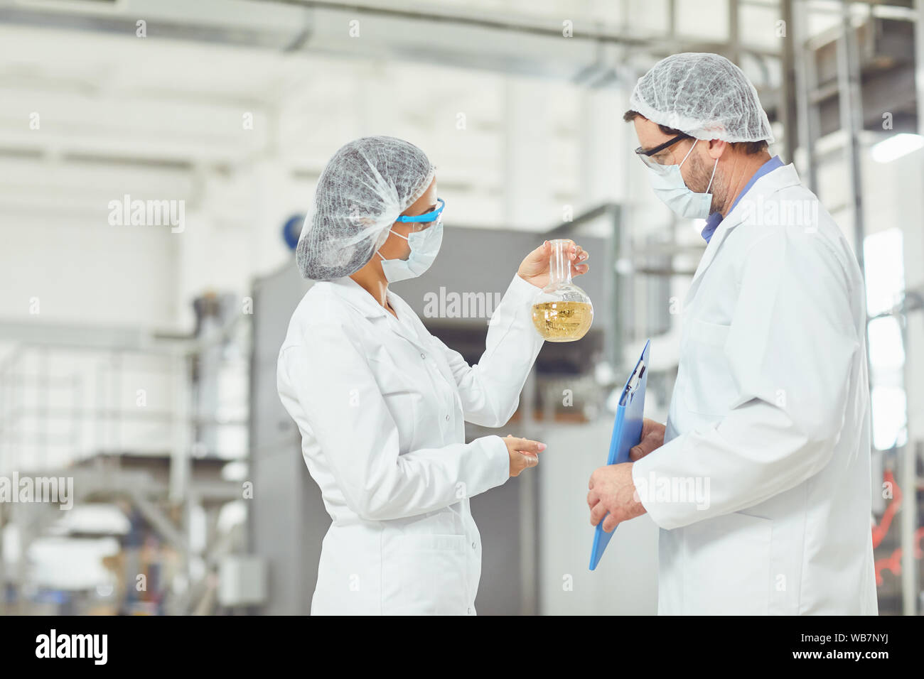 Worker in masks and coats look at the liquid in the flask at work. Stock Photo