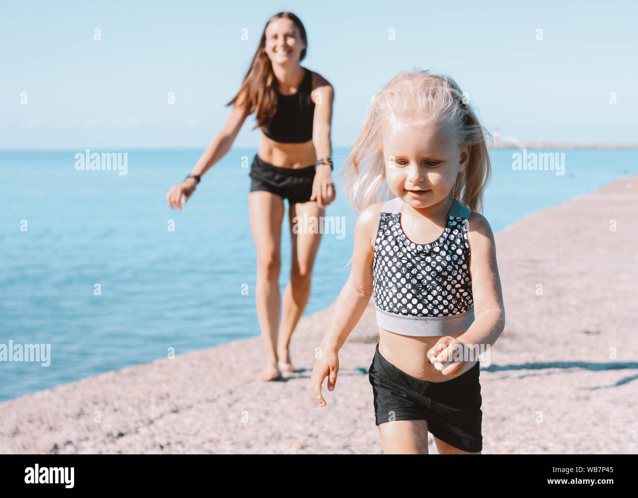 Little cute girl looking to the fit mom on beach, healthy lifestyle, sport family Stock Photo