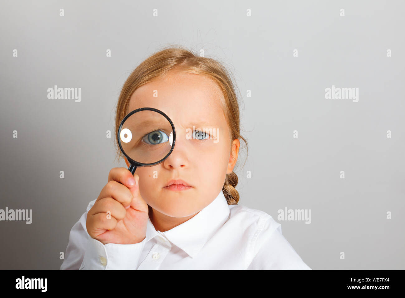 Little girl looks through an magnifying glass with interest. The concept of education, school, research, search. Stock Photo