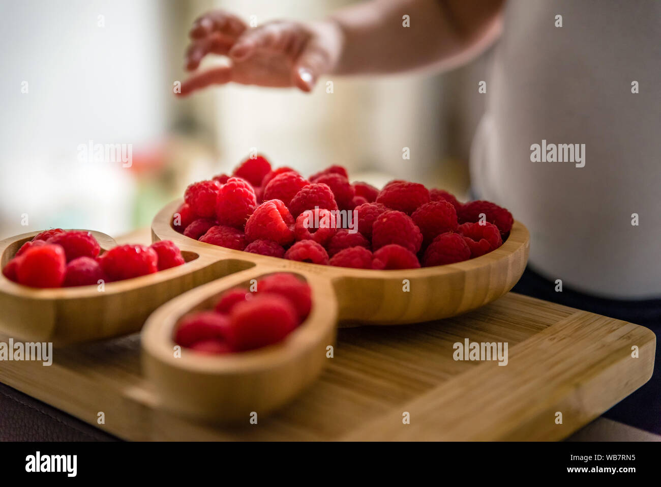 baby boy hands touch and take raw fresh raspberries on wooden bamboo ...