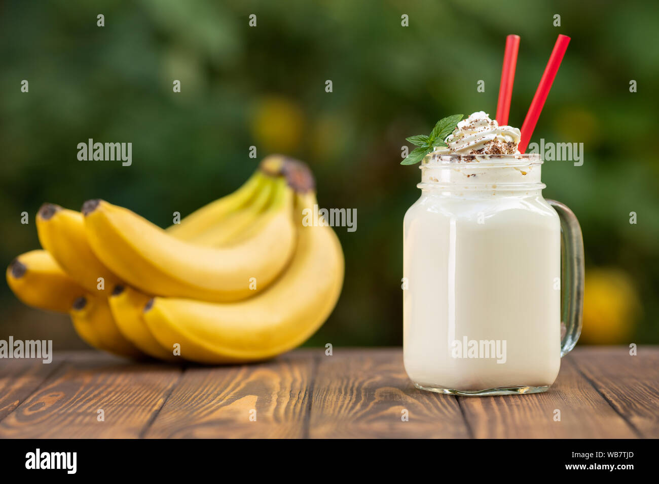 banana milkshake in mason jar with whipped cream on wooden table with green blurred natural background Stock Photo