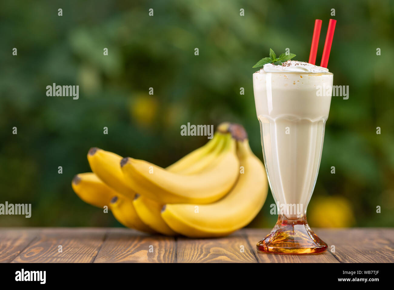 banana milkshake in glass with whipped cream on wooden table with green blurred natural background Stock Photo