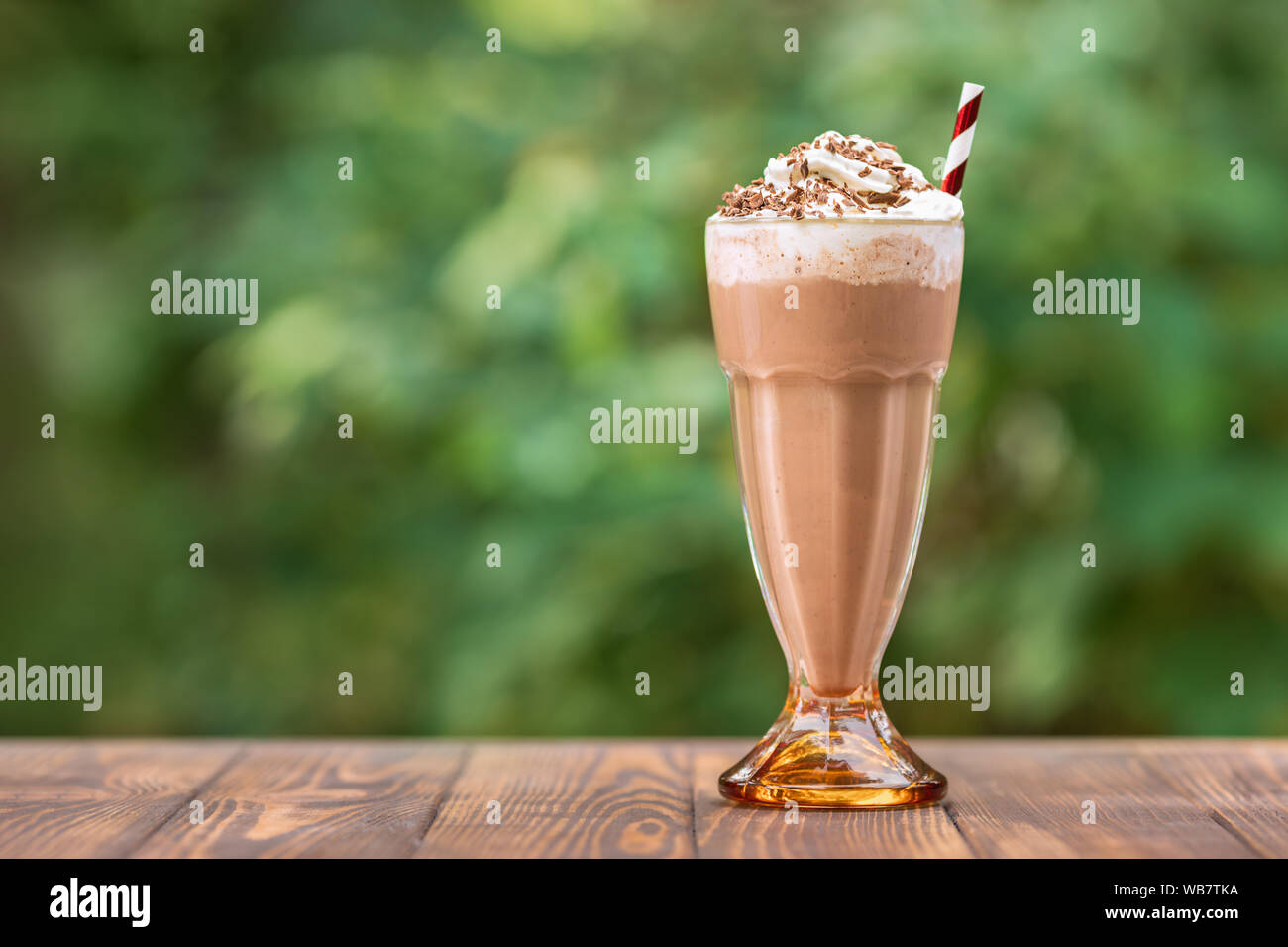 chocolate milkshake in glass with whipped cream on wooden table outdoors Stock Photo