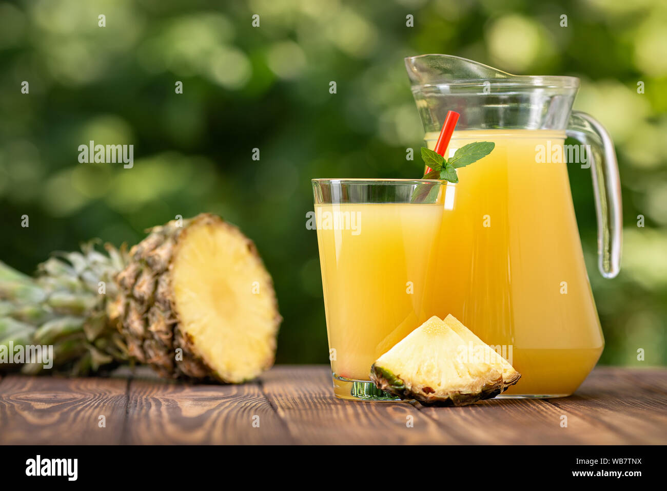fresh pineapple juice in glass and jug with ripe fruit on wooden table ...