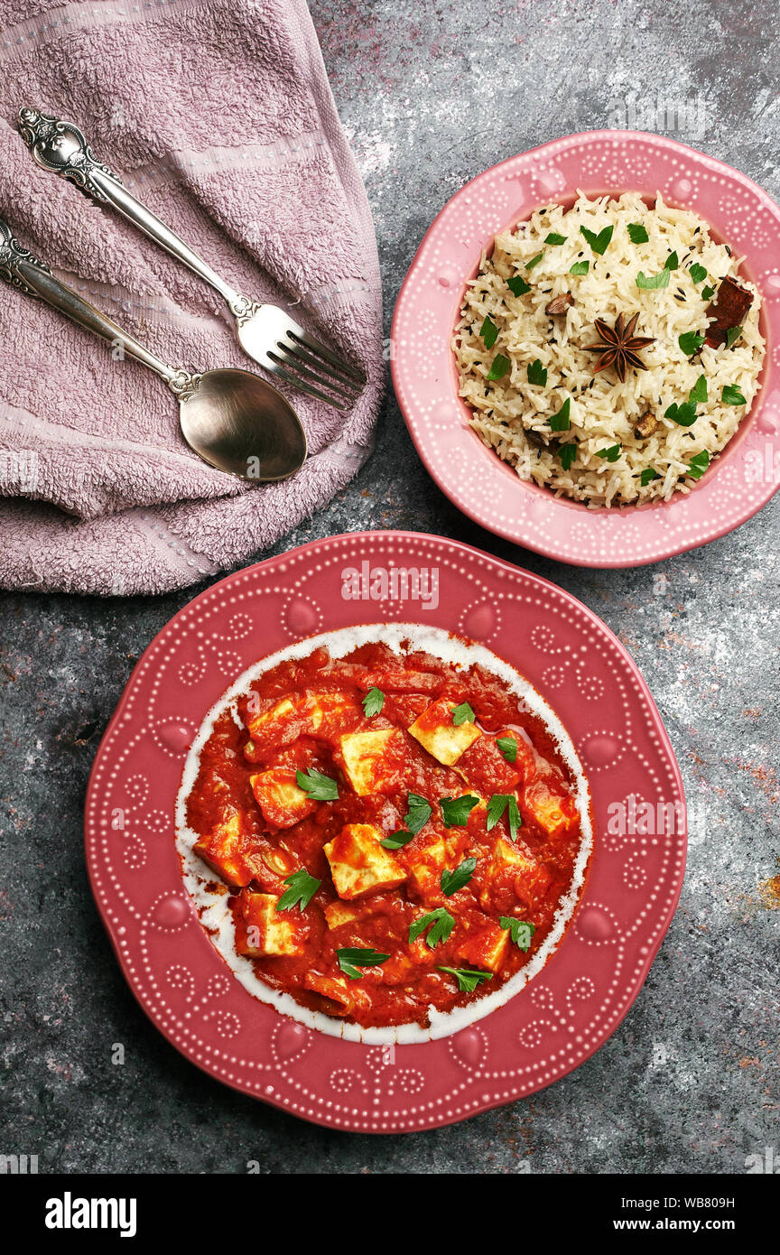 Paneer Makhani and jeera rice in pink plates on dark background. Paneer