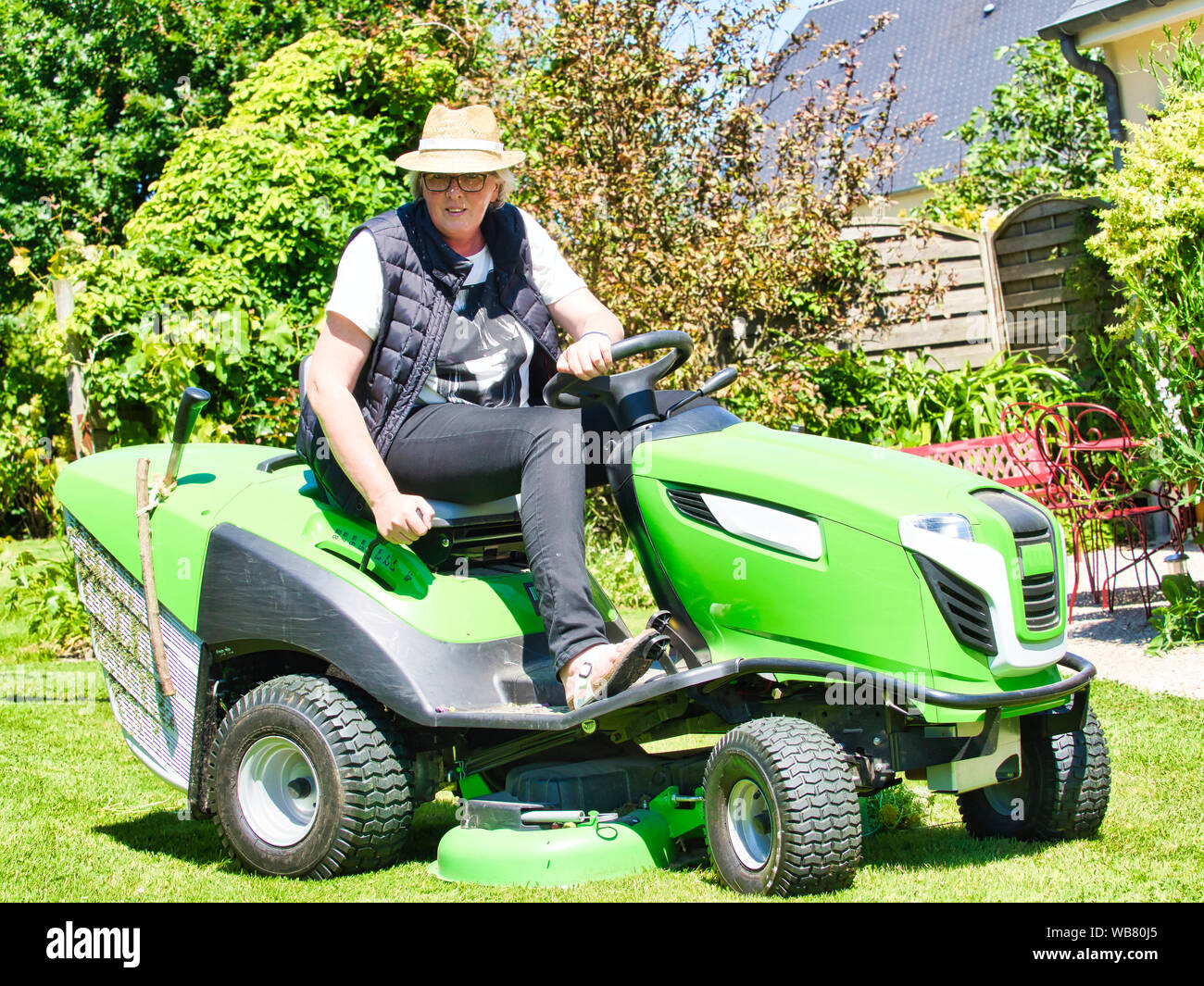 Mature Woman With Hat Driving A Tractor Lawn Mower In Garden With