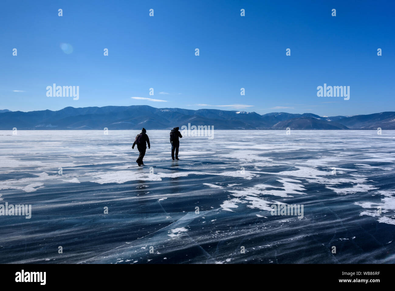 Frozen Lake Baikal. Two people silhouettes walk on the ice surface on a