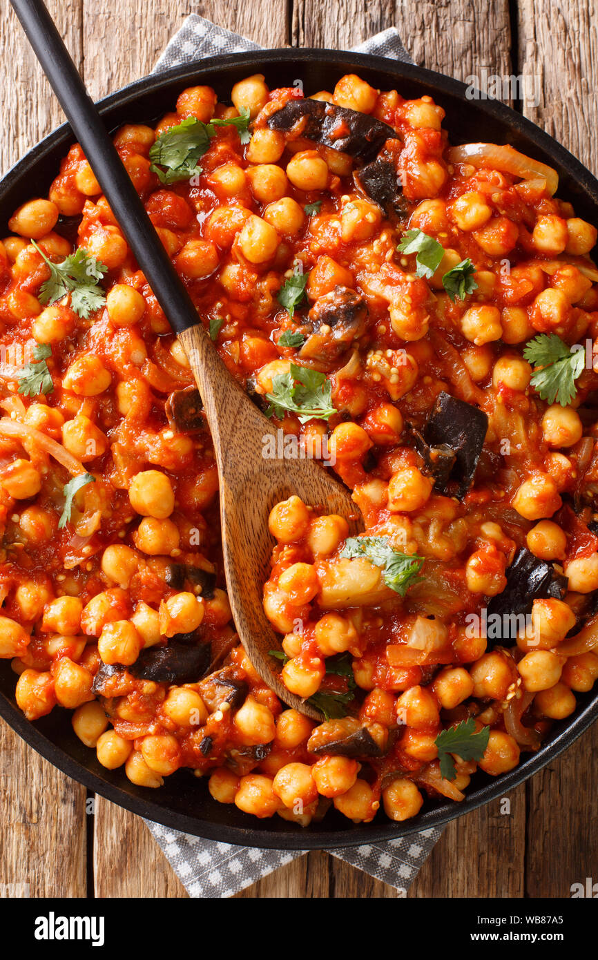 Israeli vegetarian cuisine stew of chickpeas with eggplant, tomatoes, onions and spices closeup on a plate on the table. Vertical top view from above Stock Photo